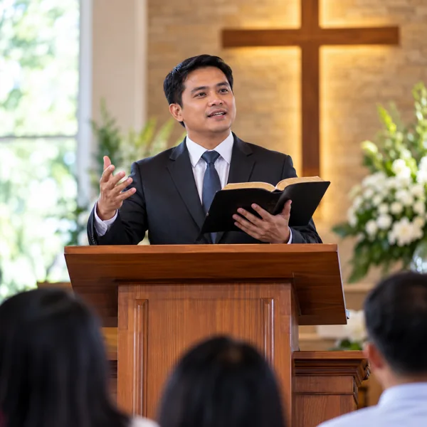 Pastor holding an open Bible while speaking from a lectern